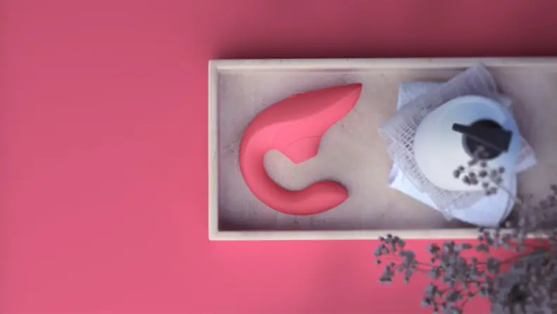 A Womanizer Blend in pink next to a lotion dispenser on a tray, with a table surface in matching pink.