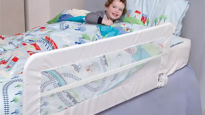 Small child in bed under covers with the Dreambaby Savoy Fold Down Bed Rail on side of bed.