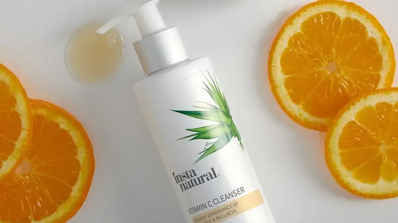 The InstaNatural Vitamin C Cleanser on a white background with orange slices surrounding it and a dollop of product pooling below the pump.
