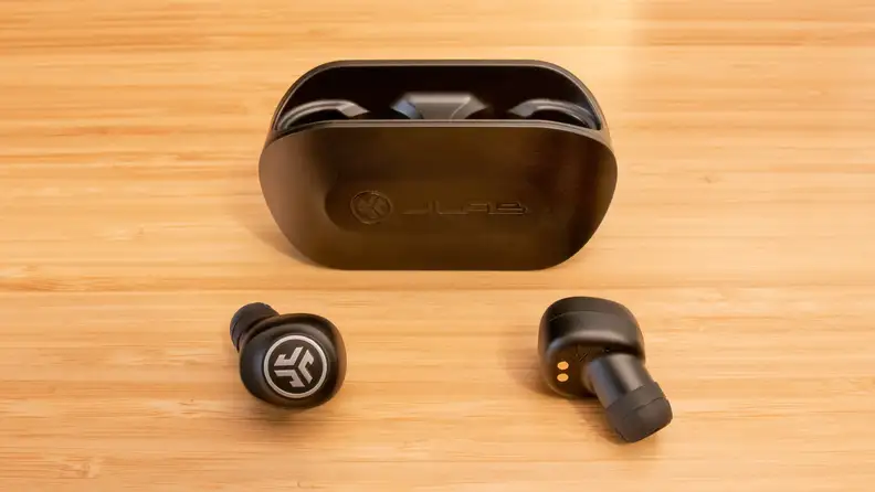 A pair of JLab Go Air earbuds and charging case on a brown table.