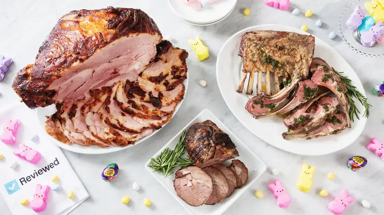 Cooked sliced ham, small lamb roast, and lamb chops on white plates are spread out on a white counter for serving.
