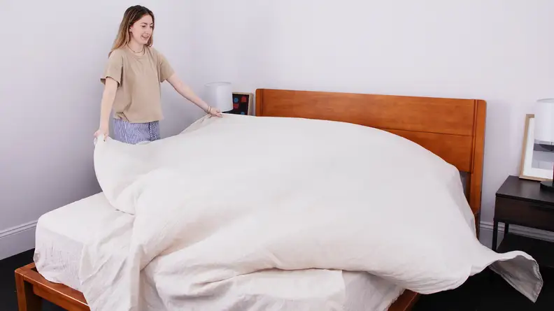 Woman floofing a linen sheet while making a bed