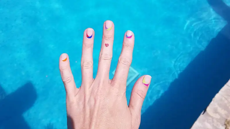 The author flexing her hand while wearing the ManiMe Es-cape Verde set. There is bright blue pool water in the background.