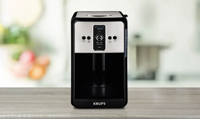 Black and silver Krups coffee maker on a wood counter