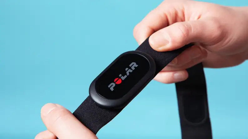 A person holding the Polar H10 heart rate monitor with a blue background.