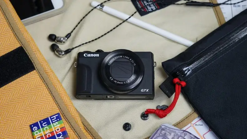 A Canon camera sits on a desk surrounded by headphones and a bag.