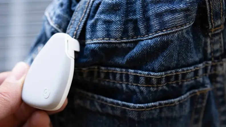 A white Jiobit tracker is attached to a belt loop on jeans.