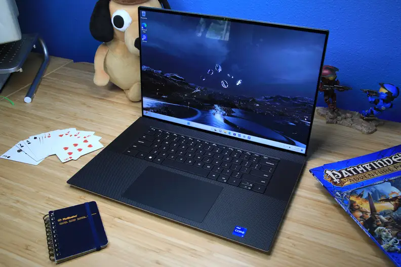 A laptop open and powered on flanked by knickknacks on top of a light brown wooden surface