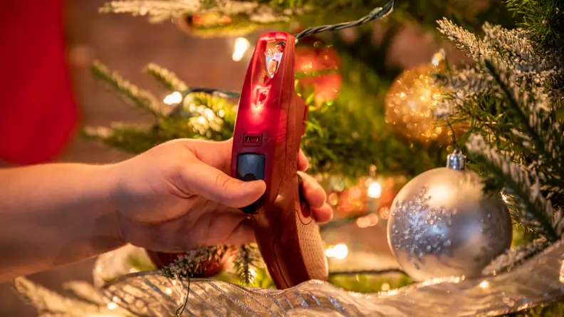 Red glue-gun-shaped gadget testing a fuse on a string light switch