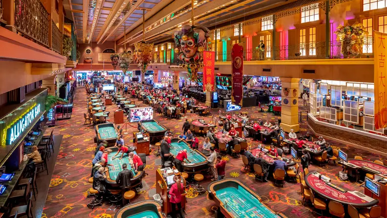 Busy Boyd Gaming casino floor featuring table games, poker tables, slot machines, and colorful Mardi Gras-inspired decor suspended above the gaming area.