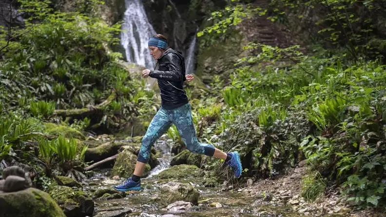 Woman wearing black Gore-Tex jacket while running in the woods.