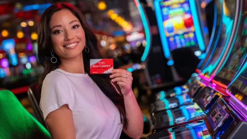 A woman wearing white shirt holding a red rewards card at the slot machines
