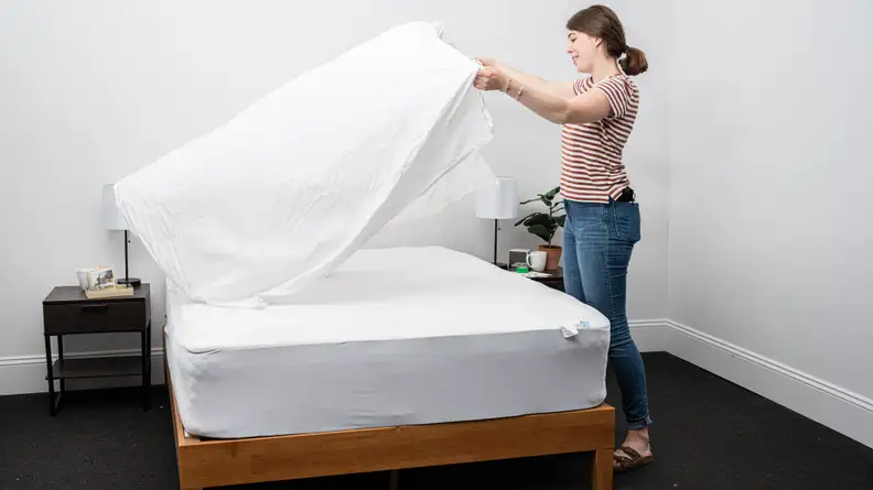 Person spreading mattress protector on bed.