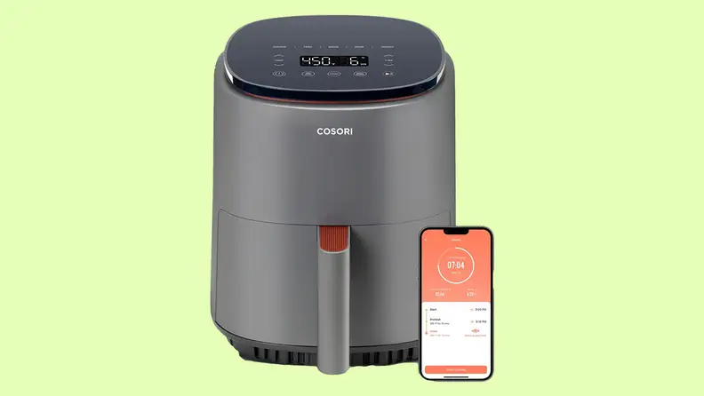 Cosori Lite four-quart air fryer with smartphone next to it in front of green background