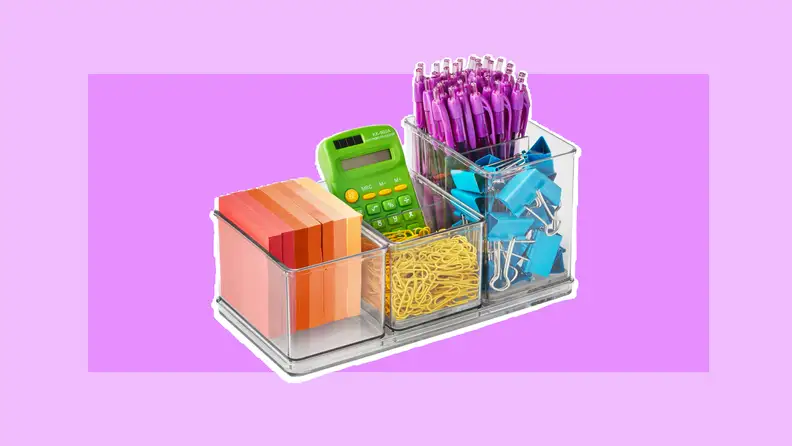 Clear acrylic desk organizer filled with multi-colored post-it notes, green calculator, purple clickable pens, yellow paperclips, and blue paper clamps.