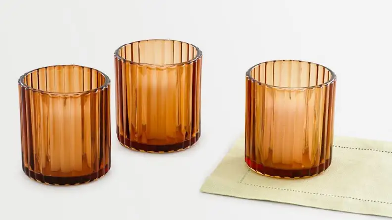 Three orange glass votives on a gray background.