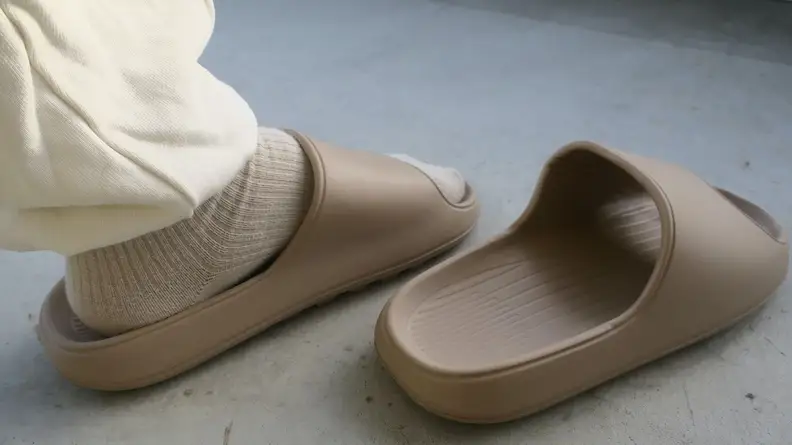 Pair of beige pool slides from Litfun, with one foot wearing a sock on the left, and one slide empty on the right.
