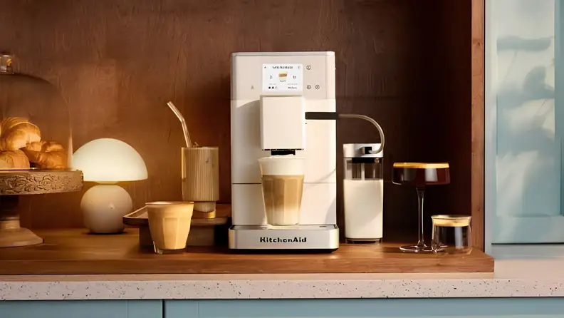 White fully automatic espresso machine preparing a milk-based coffee drink on a kitchen countertop.