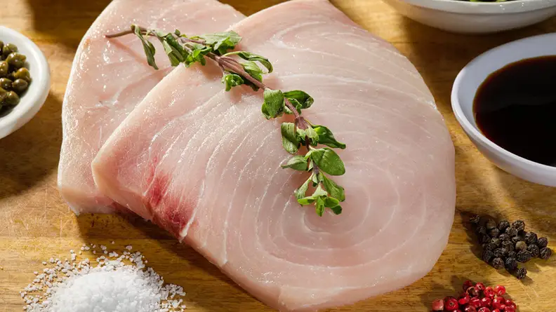 Three pieces of rainbow trout steaks on a table surrounded by salt, pepper, and other sauces.