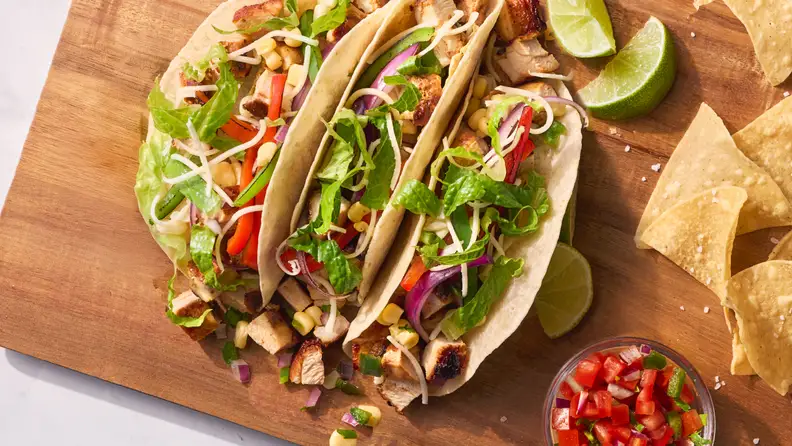 Three tacos topped with veggies, served with chips and salsa