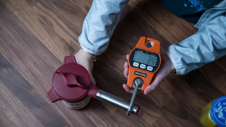 Tester demonstrates a red force meter device used to measure the strength needed for opening a sealed jar.