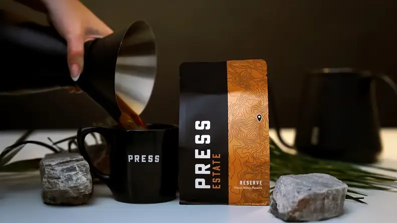Hand pouring coffee into a mug beside a coffee bag