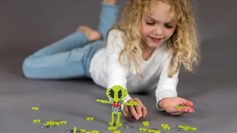 little girl building an alien out of PlusPlus blocks