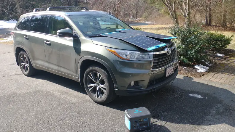 Solar panel being charged on hood of SUV on a sunny day.