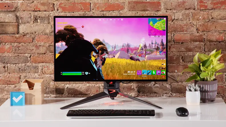Asus ROG Swift OLED PG27AQDM desktop computer on top on desk in front of brick wall.