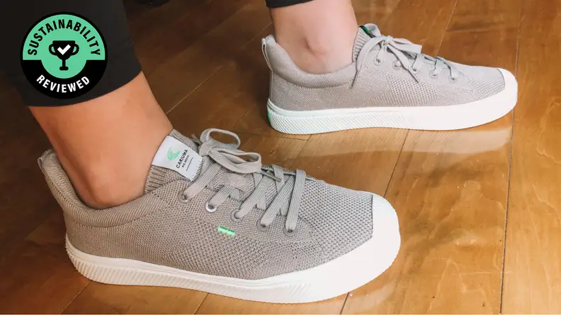 A pair of feet wearing gray and white Cariuma sneakers.