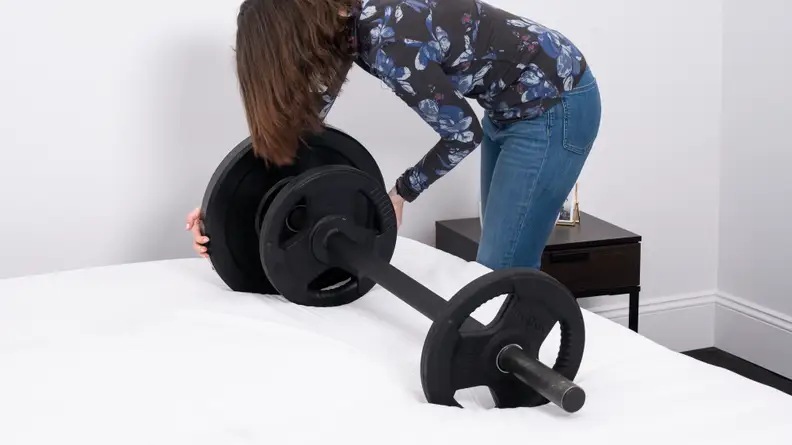 A woman stacks weights on a barbell set atop a mattress