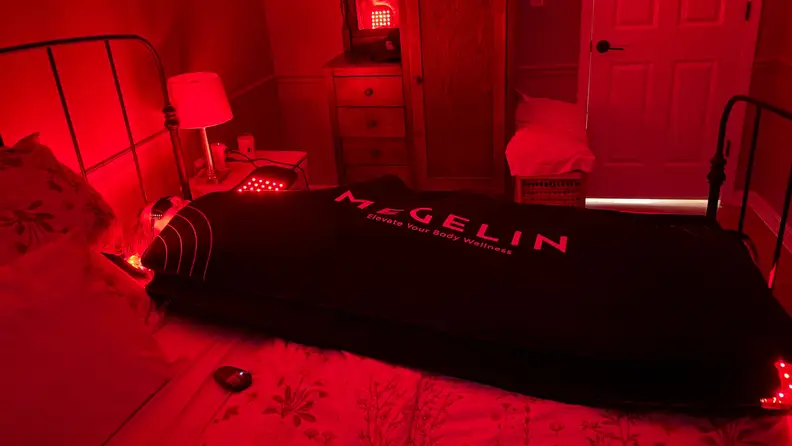 Woman laying inside the Megelin laser & LED light therapy bag with glowing red in a bedroom.