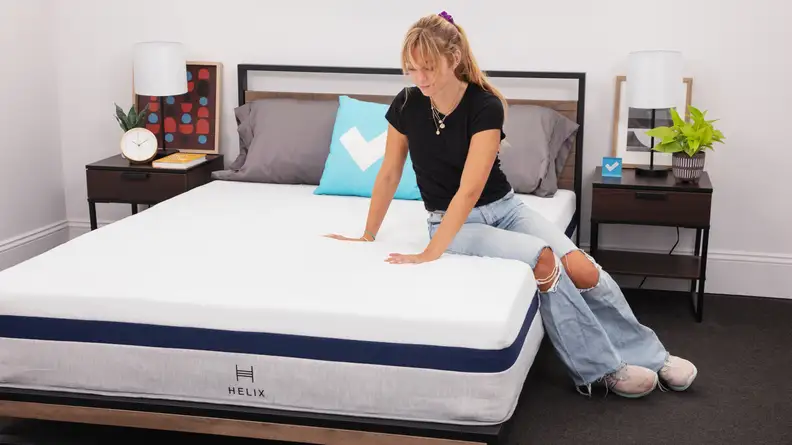 Person sitting on Helix Midnight mattress while using hands to press test the firmness.