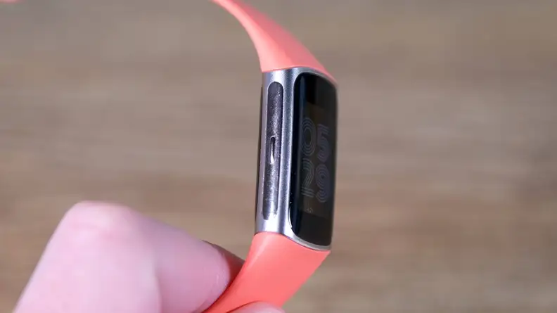 Person holding a Fitbit Charge 6 with an orange band to display the side of the watch face.
