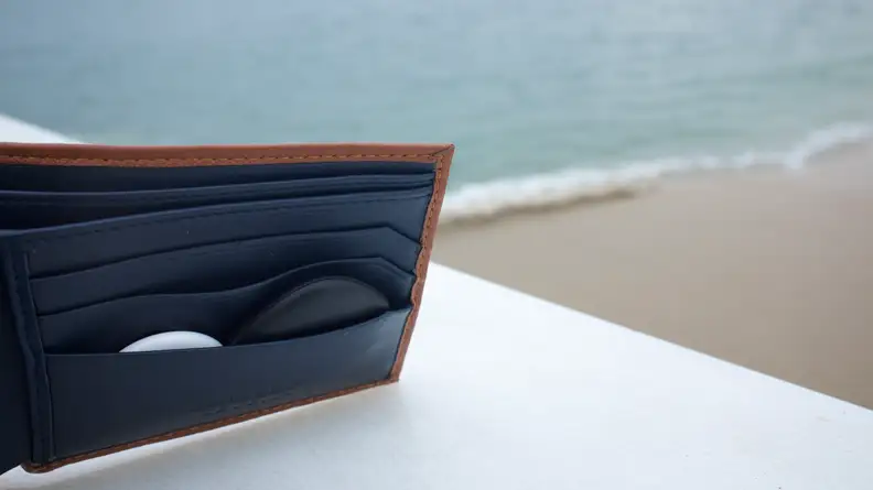 The Galaxy Smart Tag and AirTag, both tucked inside the pocket of a wallet. The Galaxy Smart Tag is sticking out significantly more, as well as bulging out more, than the AirTag.