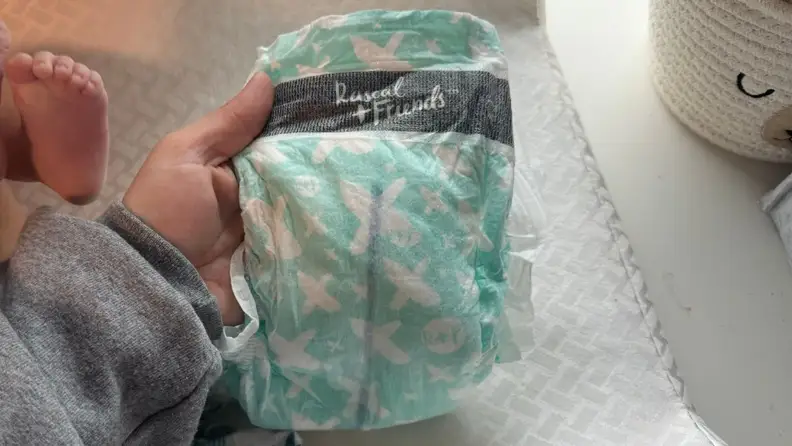 A hand holding a used diaper with the wetness indicator shown in blue.