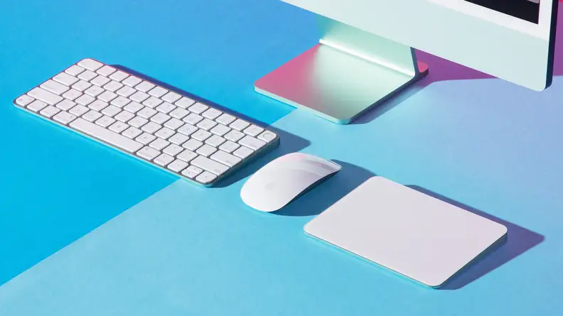 Desktop computer peripherals (keyboard, mouse, trackpad) on a blue surface.
