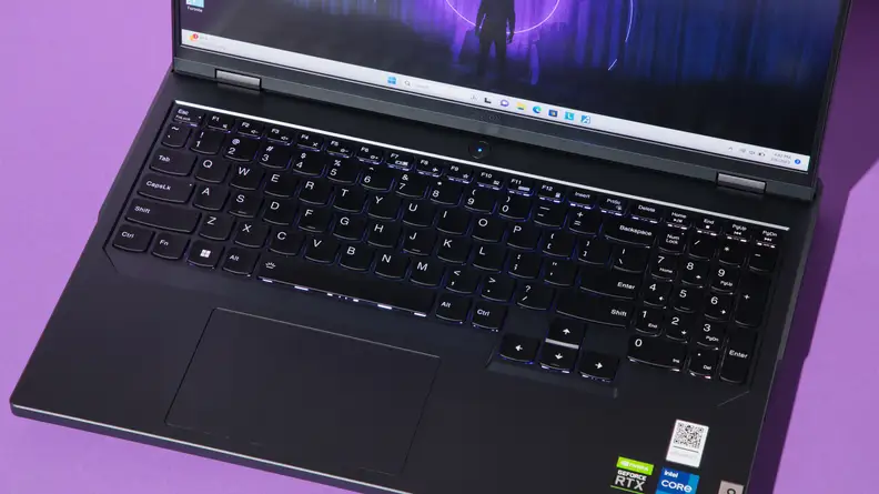 Close-up of the black keyboard and trackpad on the Lenovo Legion Pro 5i-Gen 8 gaming laptop with laptop's screen display turned on in front of purple background.