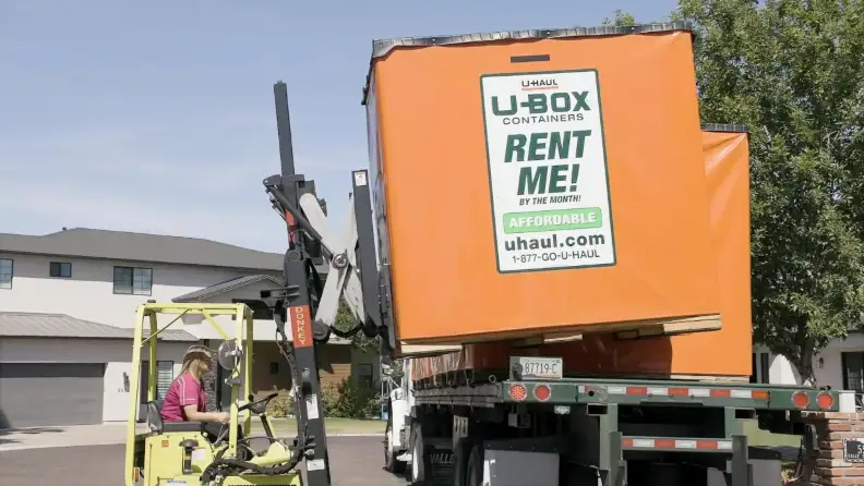 A female forklift driver unloading a small portable container box off a carrier truck