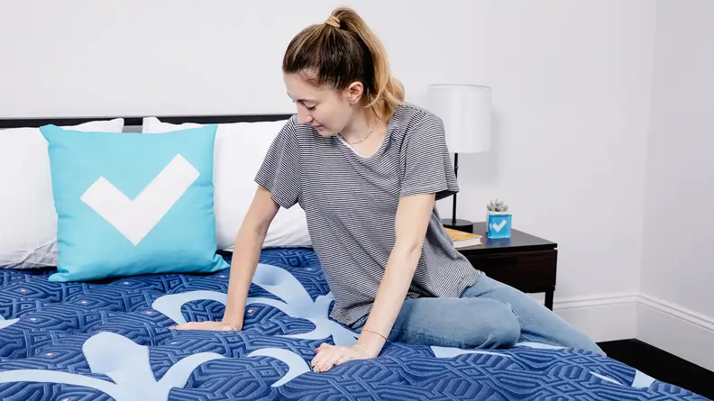 A person sitting on a mattress and pressing their hands into the surface.