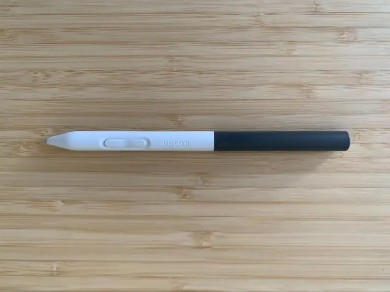 The white and gray Wacom digital drawing tablet pen appears on a bamboo desk, showing its button.