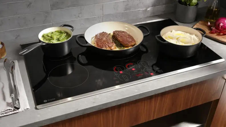 GE 36-inch induction cooktop in use cooking steaks in a skillet in a kitchen.
