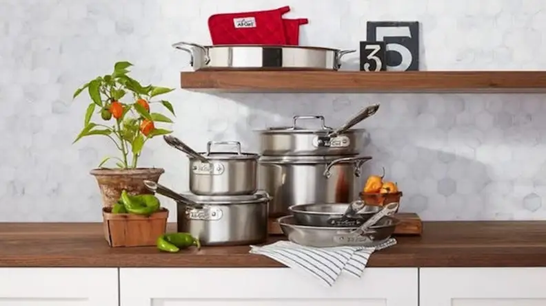 Several pots and pans are arranged neatly on a kitchen counter, along with some uncut peppers.