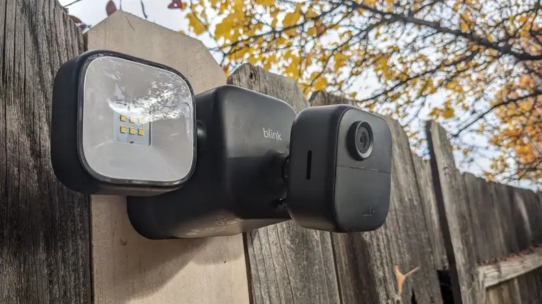 Lower view of the Blink Outdoor 4 Floodlight Camera mounted on wooden fence outdoors with two identical floodlights located on both sides.