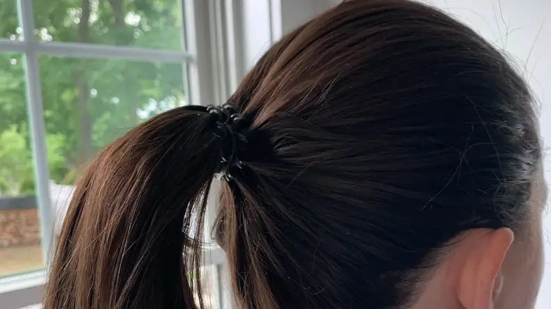 A person with long brunette hair wearing the Kitsch Spiral Hair Coil in her hair for a ponytail.