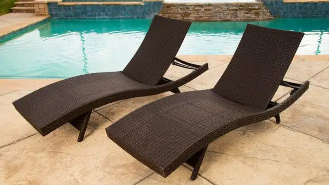 Two brown wicker patio chairs sitting on pool deck next to pool