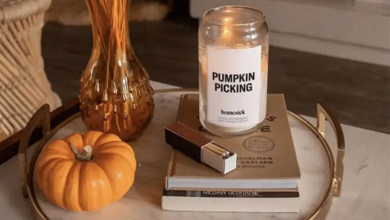 A pumpkin candle sitting on two books next to matches, a vase, and a mini pumpkin on a marble tray.