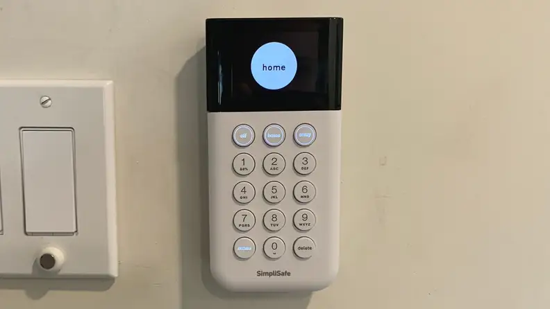 A SimpliSafe keypad hangs on a white wall.