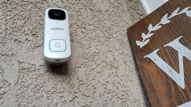 White Lorex 2K Wired Video Doorbell mounted on wall on home outdoors.