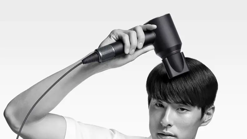 A person using the Dyson Supersonic hair dryer in front of a blank background.